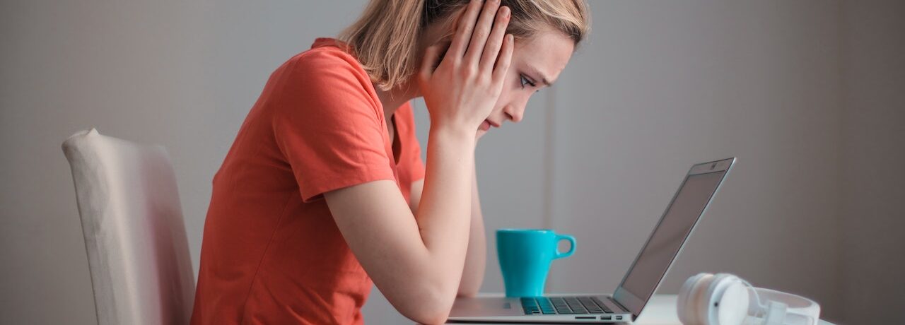 upset woman sitting at desk looking at computer after being terminated from her job