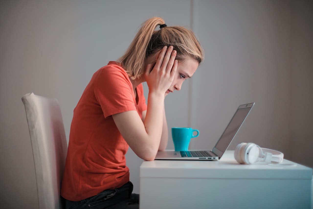 upset woman sitting at desk looking at computer after being terminated from her job