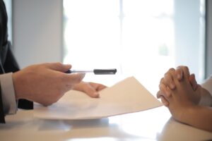 person offering document and pen to another person who has their hands folded due to unfairness of contract