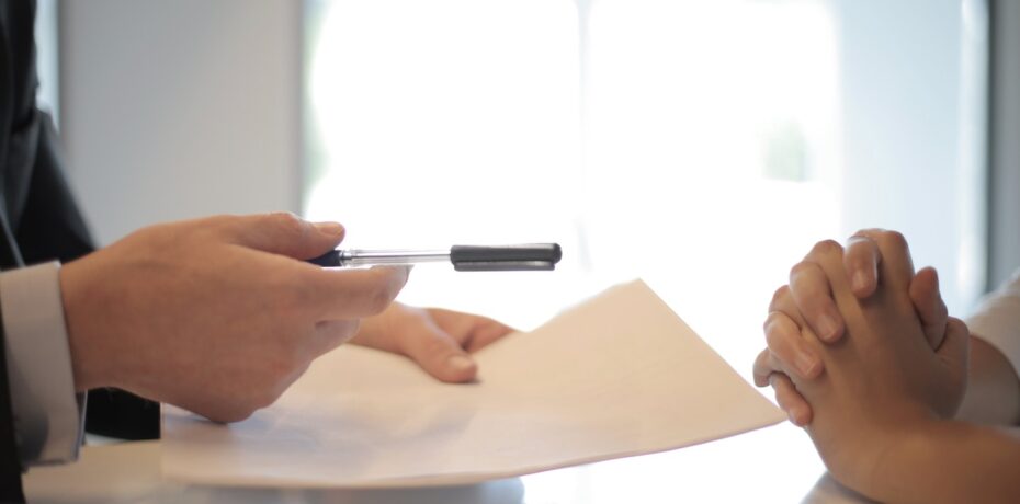 person offering document and pen to another person who has their hands folded due to unfairness of contract