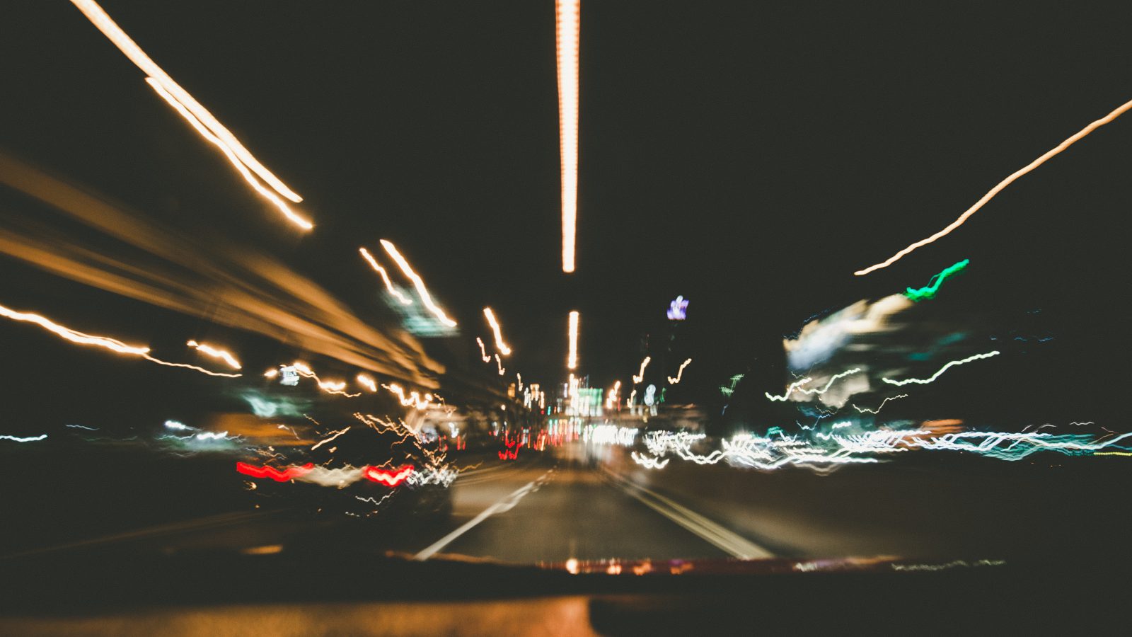 blurred streetlights seen through the windshield of a car in motion