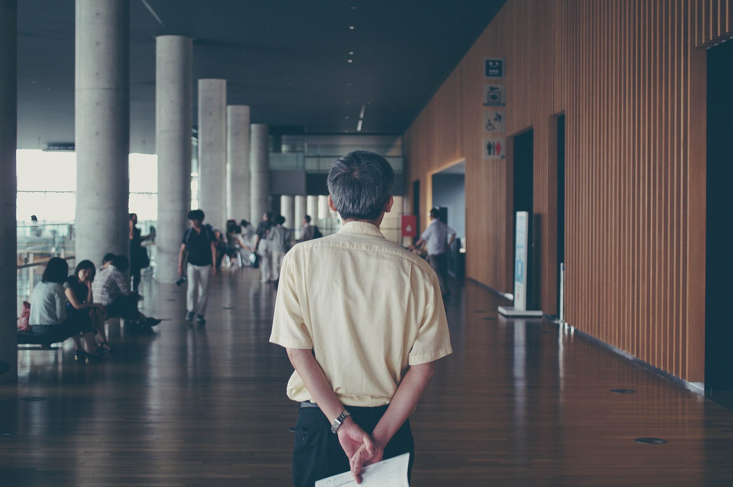 An older man standing in a university, representing an older teacher denied health benefits due to age