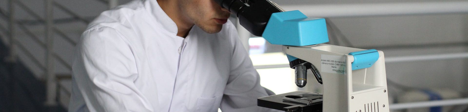 A man working in a lab using a microscope representing students doing medical research