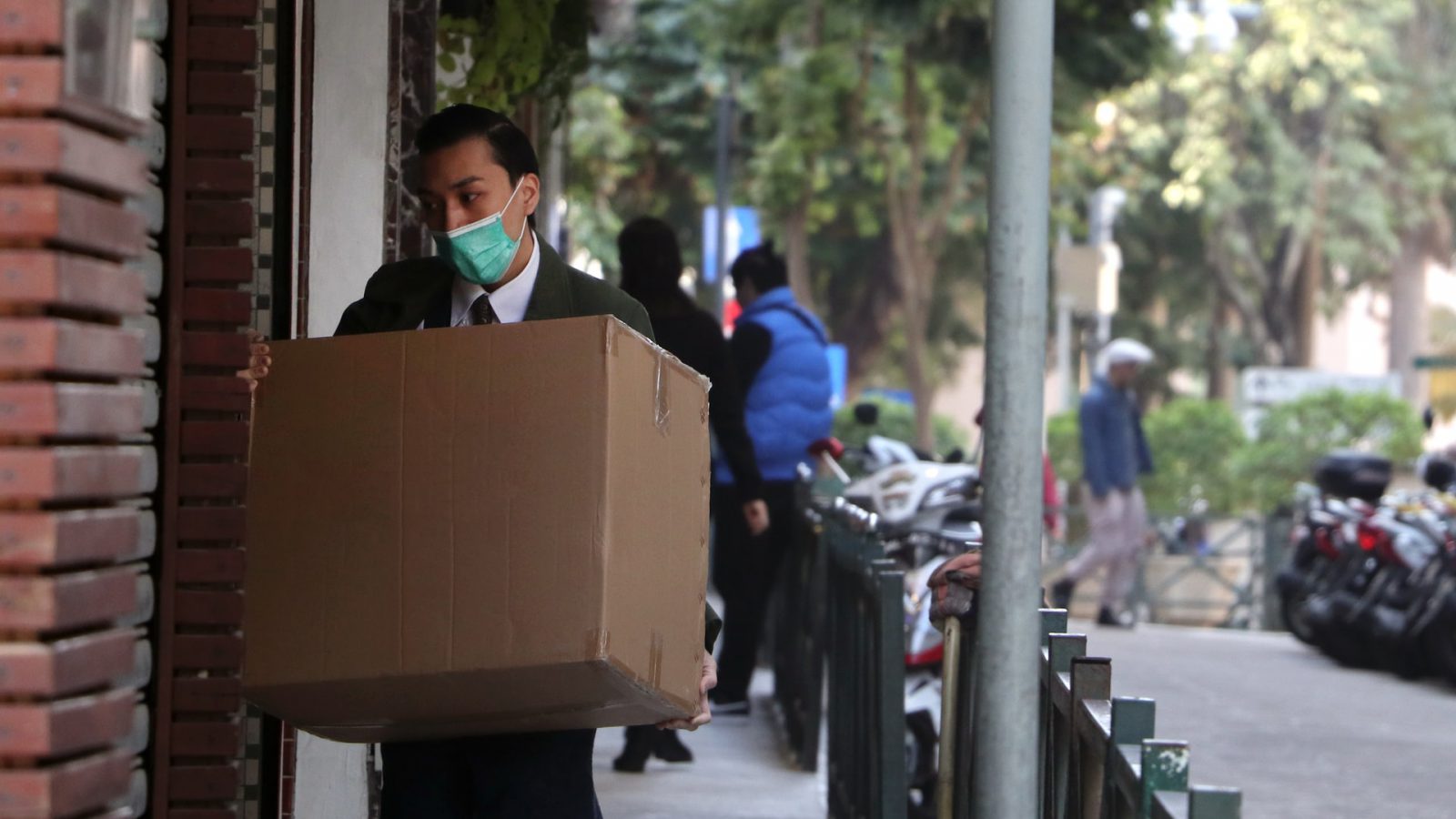 A man in a suit wearing a mask and carrying a box representing an employee let go during the pandemic