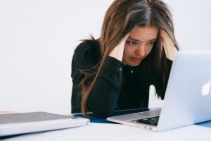 A distressed woman looking at a laptop, representing an employee who is let go due to COVID-19