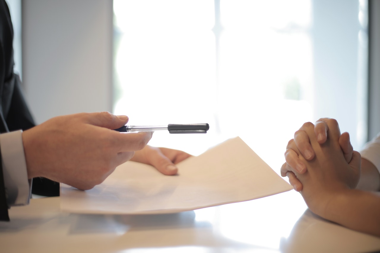 A person handing another person a pen and a contract representing an employment agreement