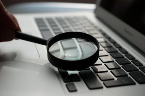 A magnifying glass on a computer, representing an employer spying on an employee's emails