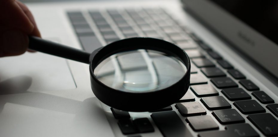 A magnifying glass on a computer, representing an employer spying on an employee's emails