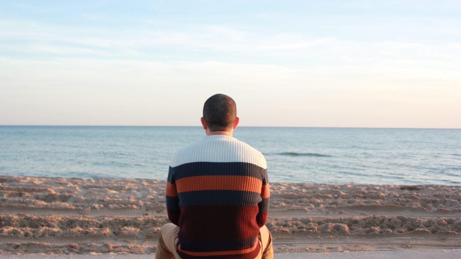man sitting on boardwalk at beach