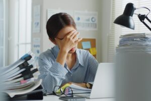 A woman sitting at her desk, surrounded by papers, holding her face in her hand, representing toxic workplaces and constructive dismissal