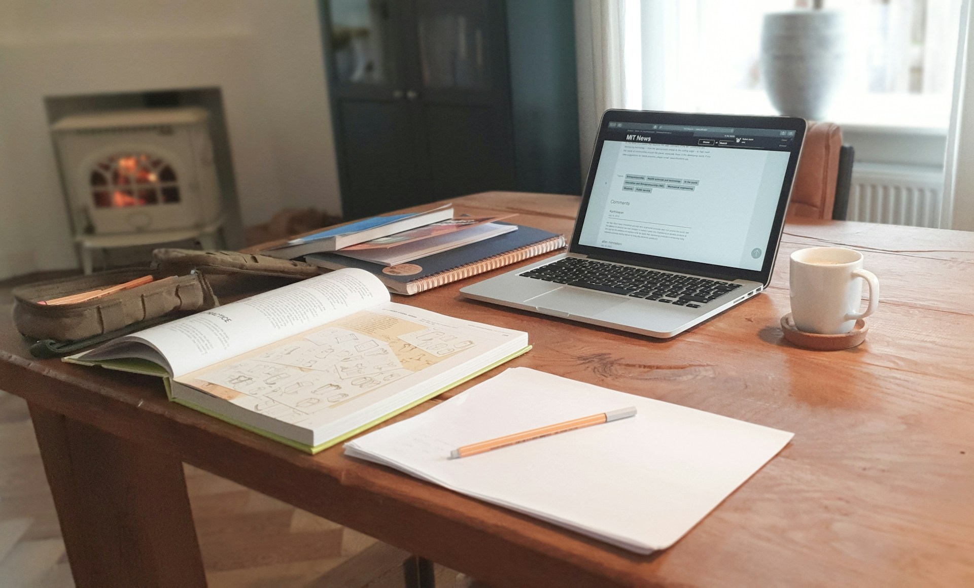A laptop and workbooks on a kitchen table with a coffee mug, representing remote work reversal.