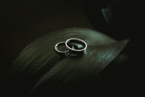A man's wedding band overlaps a woman's wedding band on a glossy, dark green plant leaf against a black background, representing divorce and employment.