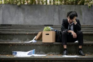 A burned-out employee sitting with a box of personal effects on some stairs, with work papers strewn about, representing being pushed out of your job (constructive dismissal or "quiet firing") in Ontario
