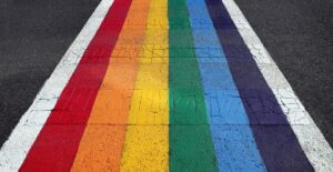 A rainbow crosswalk cuts across an asphalt roadway, representing pride-washing in employment Ontario.