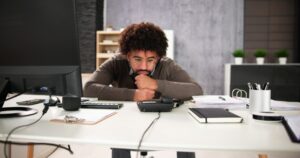 A man, sitting behind his desk, rests his chin on his stacked fists while not working, representing employee insubordination in Ontario.